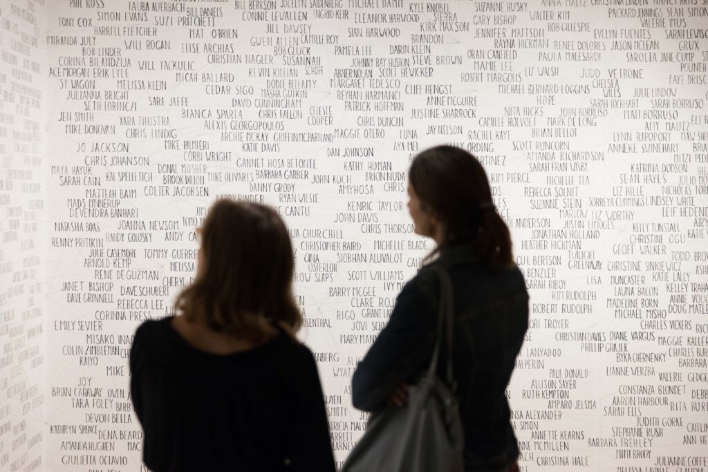 Two women in silhouette in front of a large word-art wall drawing