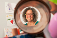 A smiling woman looks through a tube at the camera
